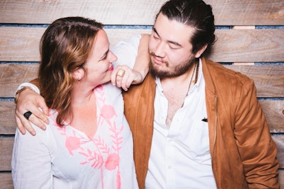A woman in a white-peach top leaning her elbow on a man in a white shirt and camel blazer and they'r...