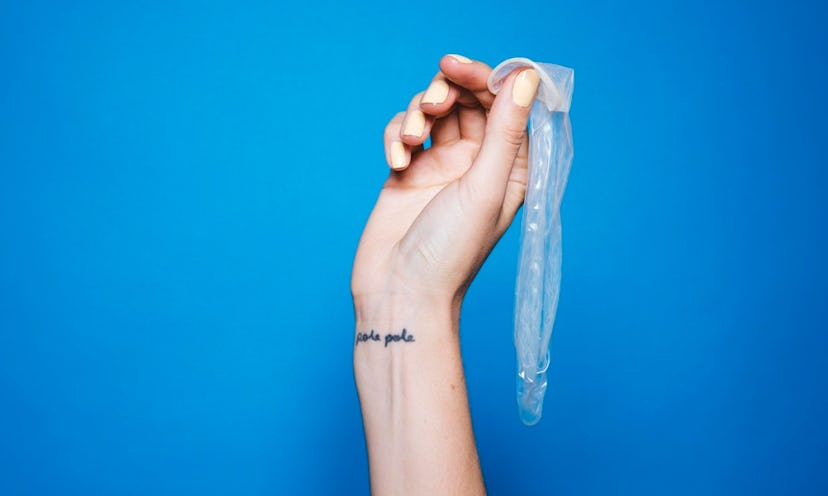 A woman's hand holding a used condom with a blue background