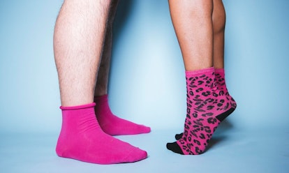 A man's feet in pink socks facing and a woman's feet in black and pink leo print socks standing tipt...