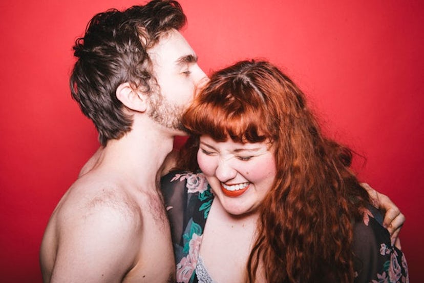 A topless man kissing a redhead woman in a floral gown