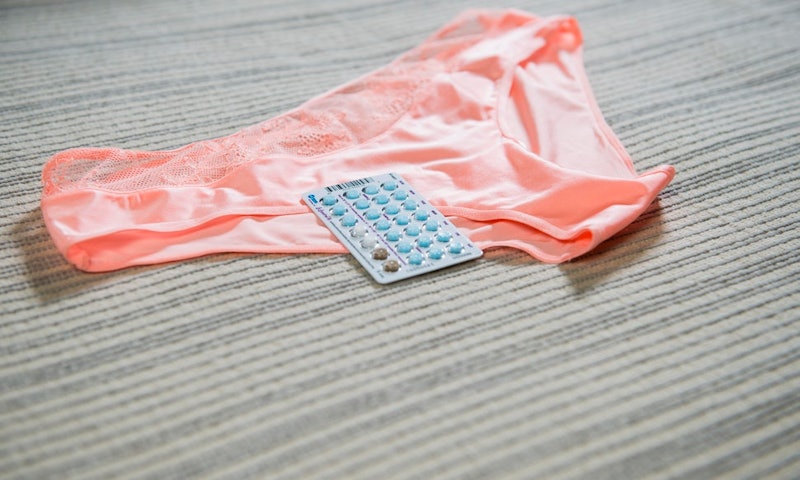 Light orange panties and package of birth control pills on a beige surface