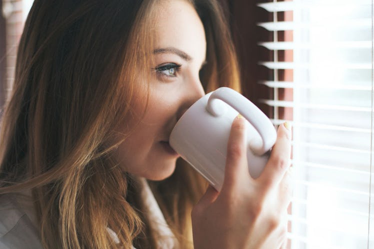 A woman drinking coffee, looking at the sunlight from her window as it has health benefits