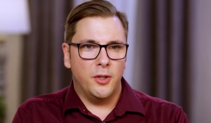 Col from '90 Day Fiance' in a burgundy shirt and black glasses