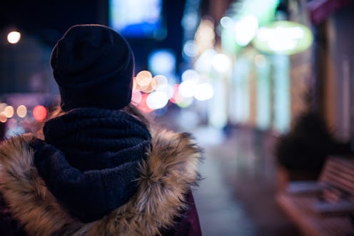 A woman with breast cancer standing out on the street at night during the winter in her coat