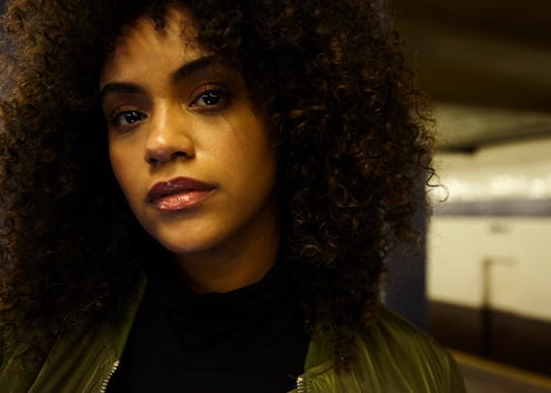 Hannah baxter in a black leather jacker and a black top standing on a subway platform