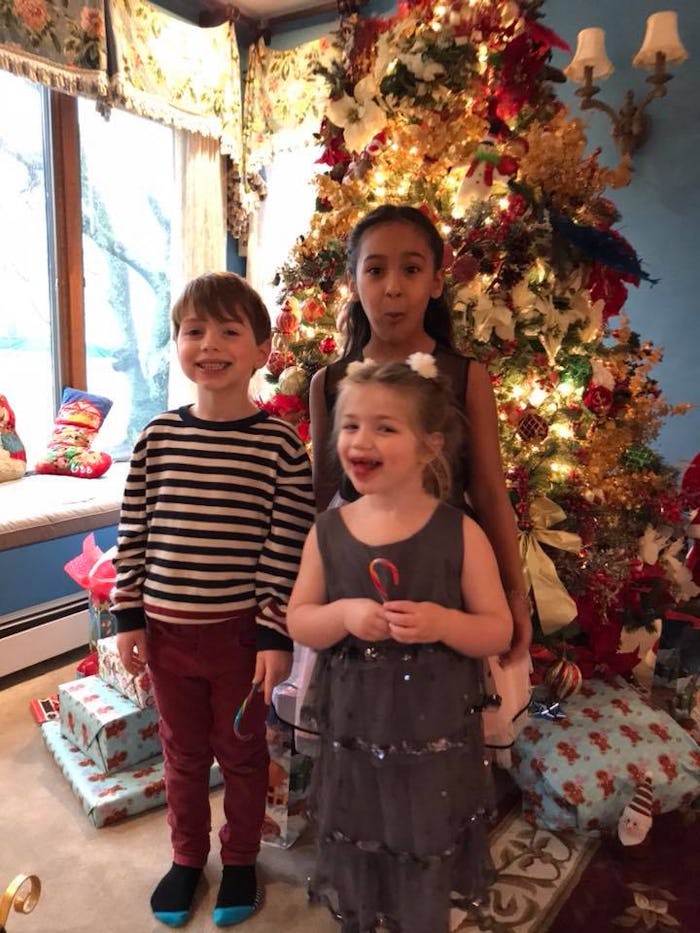 Three kids standing in front of a Christmas tree at home, laughing and making silly faces