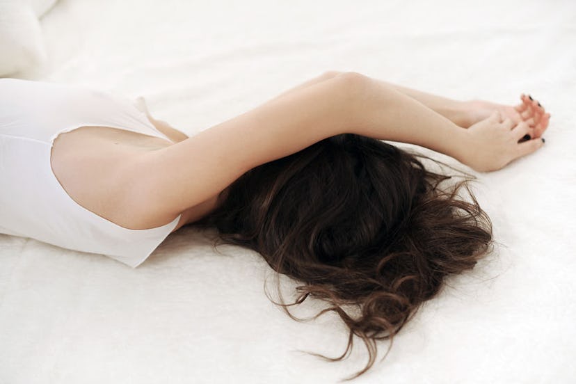 A brunette woman lying down depressed in a bed
