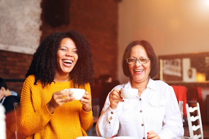 A mother and daughter enjoy coffee at a café while laughing.