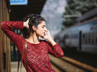 A woman leaning against a wall, making a doctor's appointment on her phone