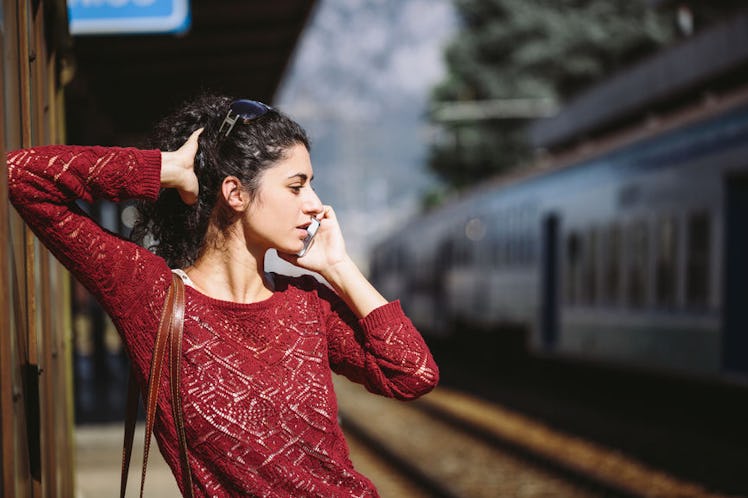 A woman leaning against a wall, making a doctor's appointment on her phone