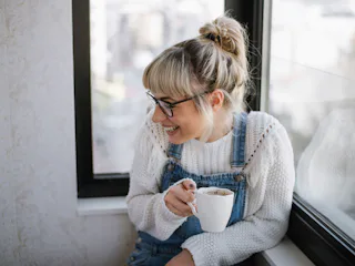 A young female smiling and holding a cup of coffee.