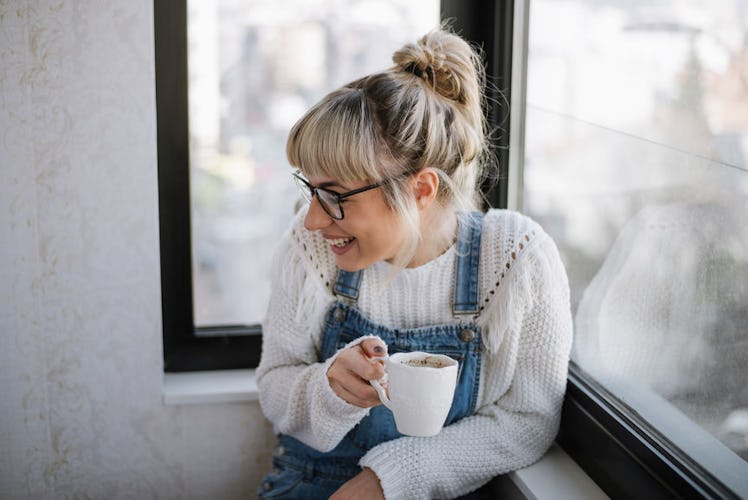 A young female smiling and holding a cup of coffee.