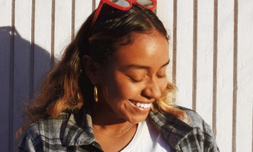 Evelynn Escobar smiling while looking on the side in front of the white background during a sunny da...