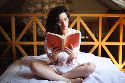 A young woman sitting on her bed reading a book