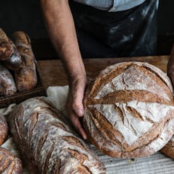 A baker holds bread on a wooden table full of different types of bread.