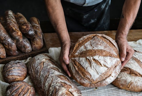 A baker holds bread on a wooden table full of different types of bread.