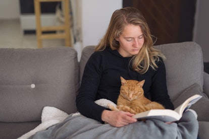 A young woman with a cat on her lap reading a book