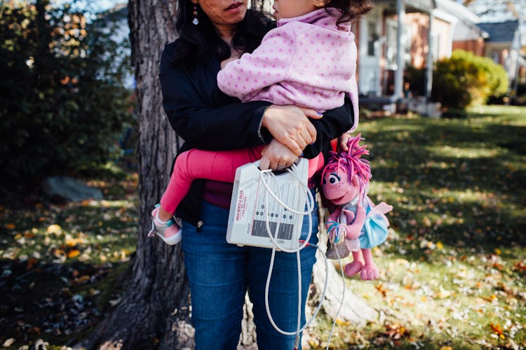 Elena carrying her daughter Xiomara and Xiomara's pulse oximeter