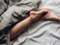 A pair of female legs in bed covered in dark gray sheets as she sleeps in separate beds from her par...