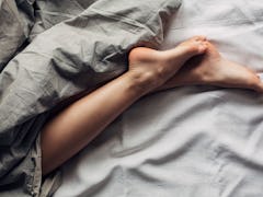 A pair of female legs in bed covered in dark gray sheets as she sleeps in separate beds from her par...