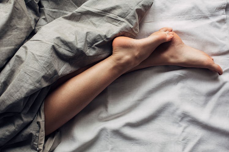 A pair of female legs in bed covered in dark gray sheets as she sleeps in separate beds from her par...