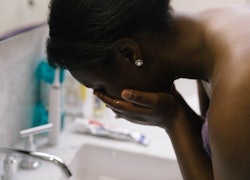 A woman washes her face in a bathroom.