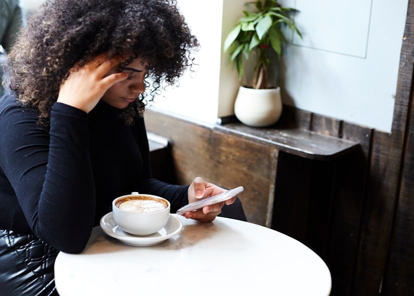 Woman sitting in a café looking at her phone, struggling to remember a word