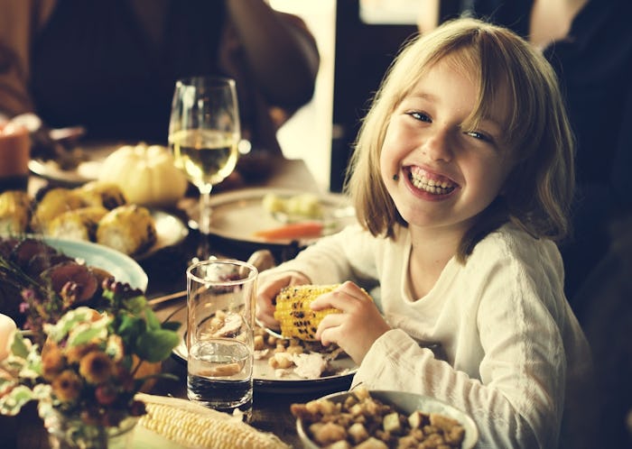 a smiling little girl sitting at the thanksgiving dinner table