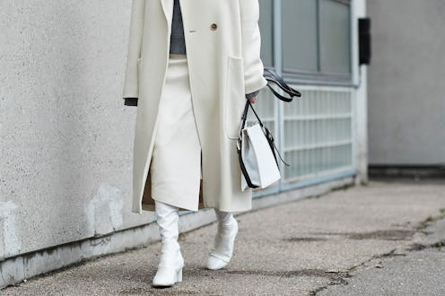 A woman wearing a white coat, skirt and boots, and a grey sweater from a winter capsule wardrobe