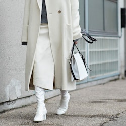 A woman wearing a white coat, skirt and boots, and a grey sweater from a winter capsule wardrobe