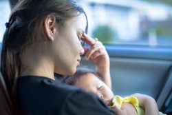 A woman with Physical Symptoms Of PMADs holding her newborn baby while sitting in the car