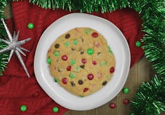 A Christmas cookie served on a plate with a red blanket beneath and green tinsel garland around it