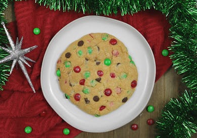 A Christmas cookie served on a plate with a red blanket beneath and green tinsel garland around it