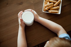 A kid with a milk alergy holds a glass of milk which is next to a plate of cookies