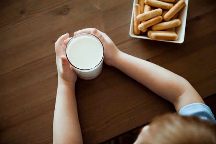 A kid with a milk alergy holds a glass of milk which is next to a plate of cookies
