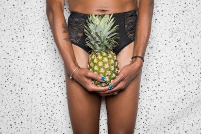 A woman in black laced underwear who has experienced pain during sex holding a pineapple over her ge...