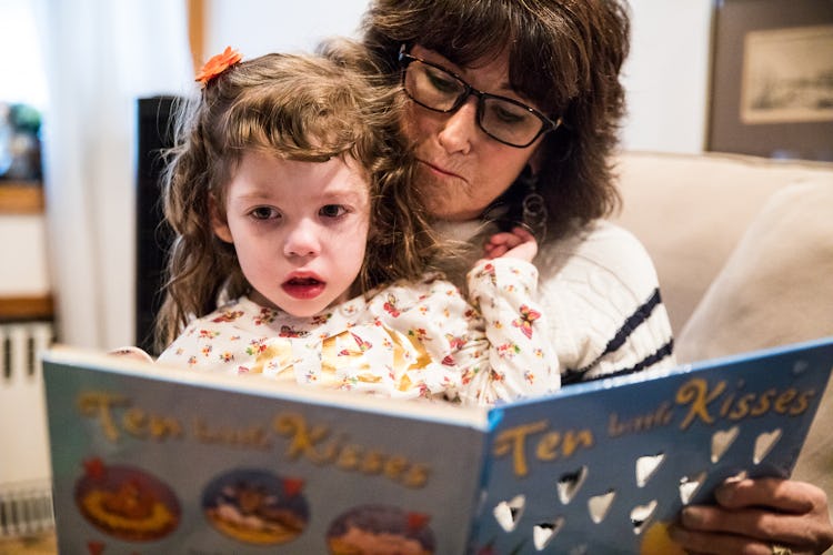 A woman is holding a little girl who has Epilepsy in her lap while they're reading a book.