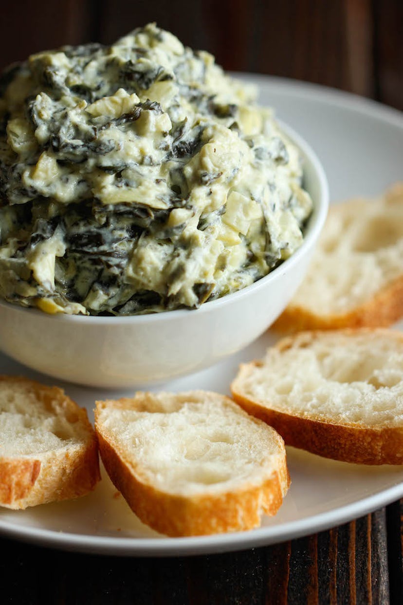 close up of bowl of artichoke dip with sliced baguette on the side