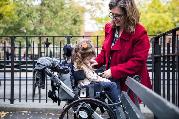 A woman positioning a little girl in a wheelchair.