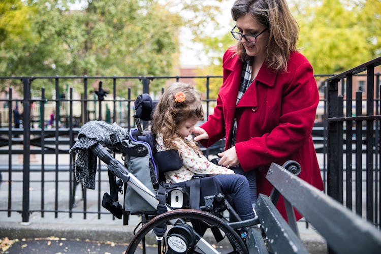 A woman positioning a little girl in a wheelchair.