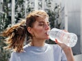 A woman with a ponytail drinking water from a bottle as a home remedy for her headaches
