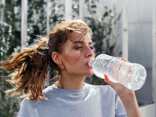 A woman with a ponytail drinking water from a bottle as a home remedy for her headaches