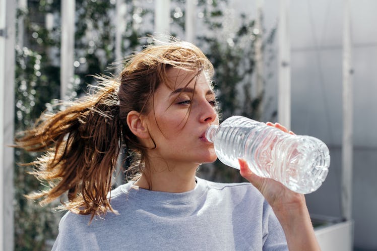 A woman with a ponytail drinking water from a bottle as a home remedy for her headaches