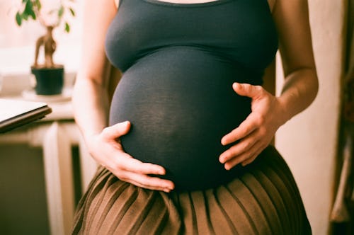 A closeup of a pregnant women's belly, with her hands holding onto the belly 