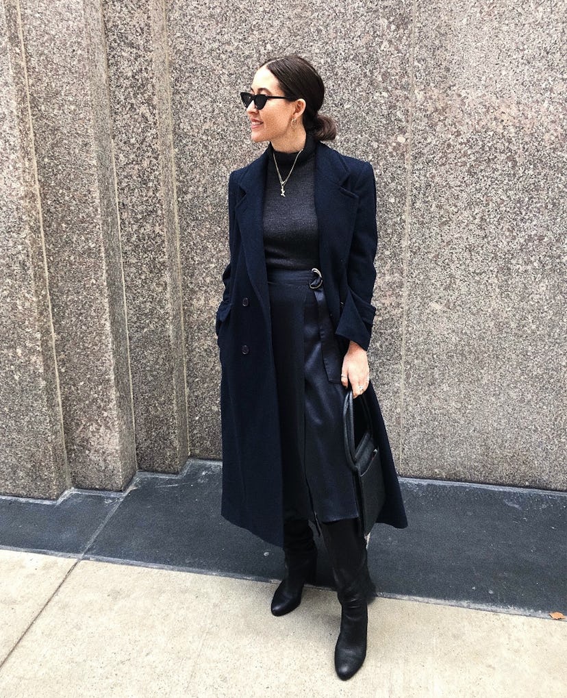 A woman posing in a black coat, shirt, skirt, and shoes combination