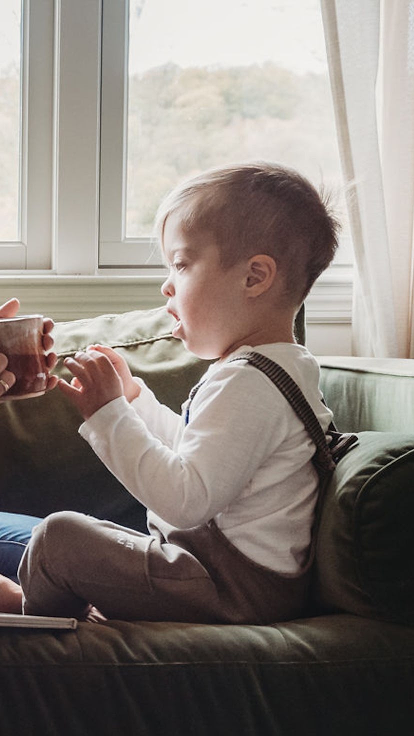 A mother drinking from a cup while smiling and sitting on a couch with her child with down syndrome