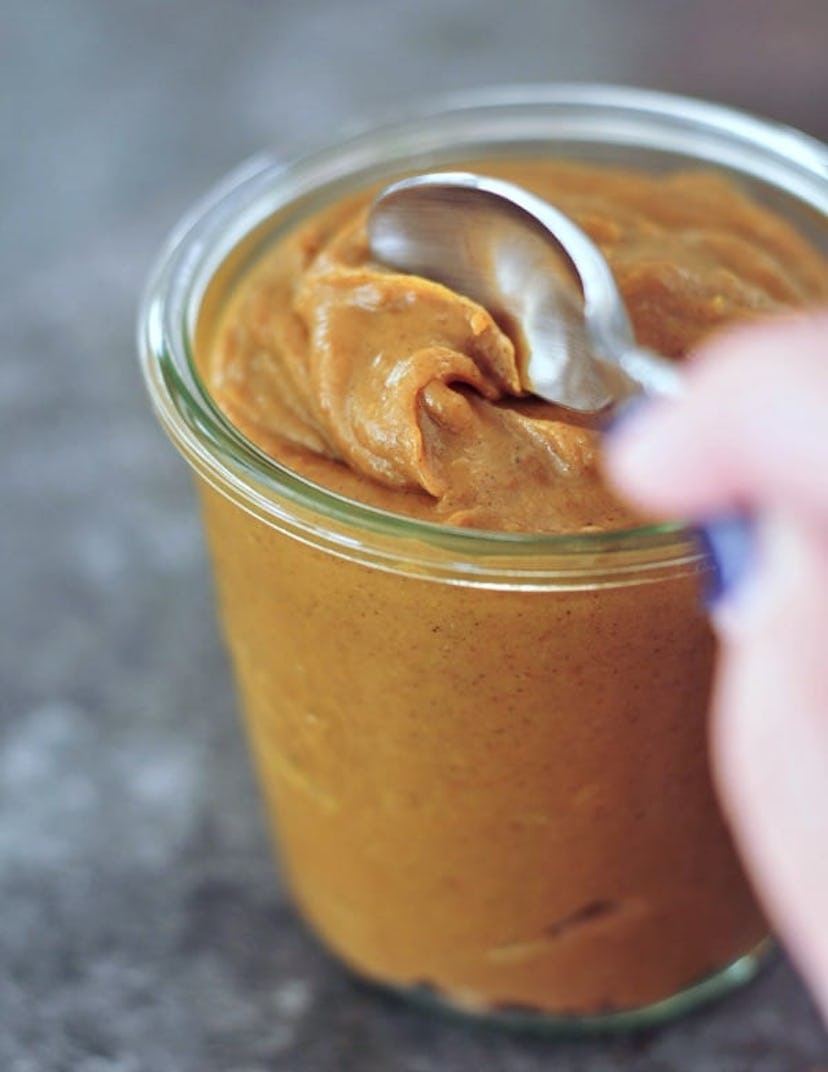 close up of glass jar with spoon scooping a brown peanut butter looking consistency
