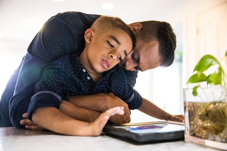 A father hugging his son while the kid looks at the tablet. 