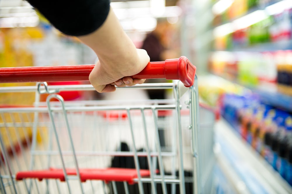 view of a shopping cart going down a grocery store aisle from behind