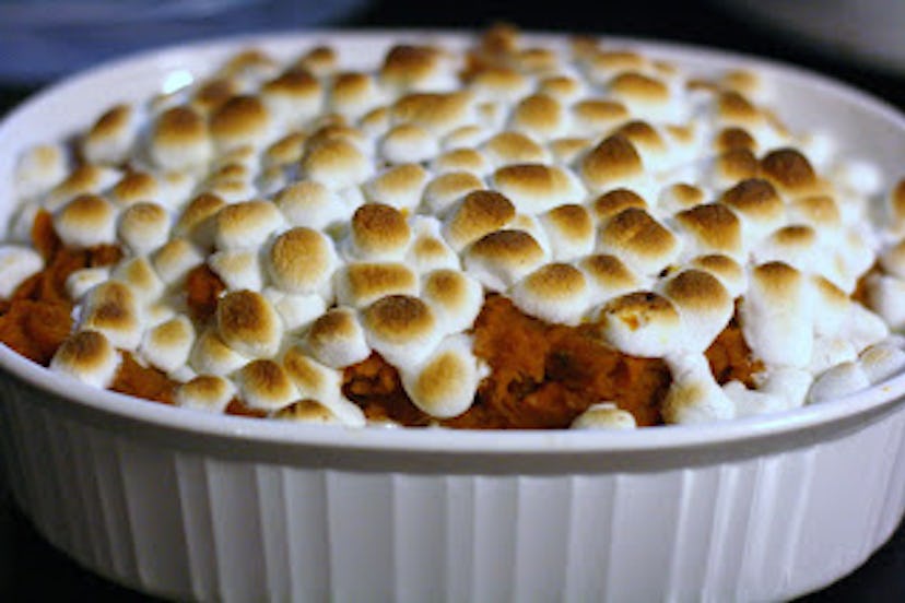 white porcelain bowl full of sweet potatoes with burnt marshmallows on top